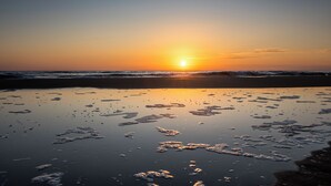 Una playa con el sol poniéndose sobre el horizonte, reflejándose en la arena mojada.