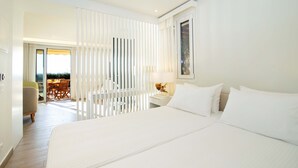 Habitación de hotel con una cama grande, una mesita de noche con lámpara, una silla y vistas a la terraza exterior.