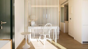 Habitación moderna con escritorio blanco, silla y lámpara. Se ve una puerta a la izquierda y una pared blanca con líneas verticales.