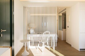 A modern room with a white desk, chair, and lamp. There is a door on the left and a white wall with vertical lines. - Glyfada Glow Suites by Corfuescapes (Corfu)