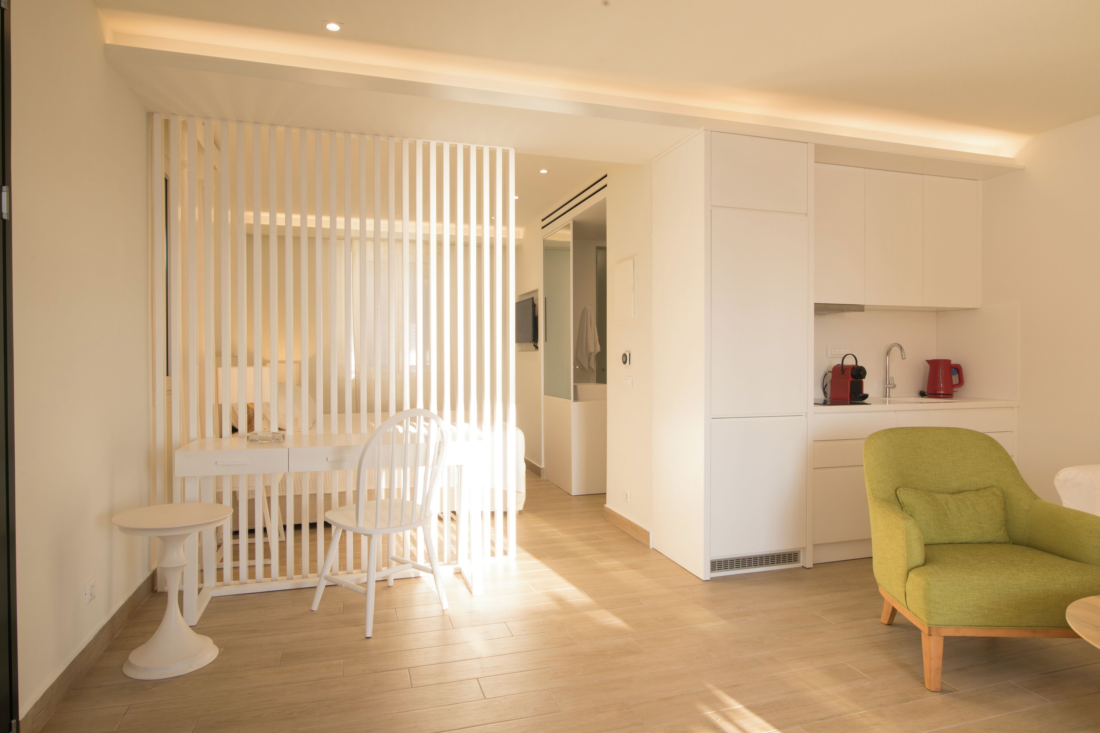 Una cocina moderna con armarios blancos, un comedor con mesa y sillas blancas, y un sillón verde.