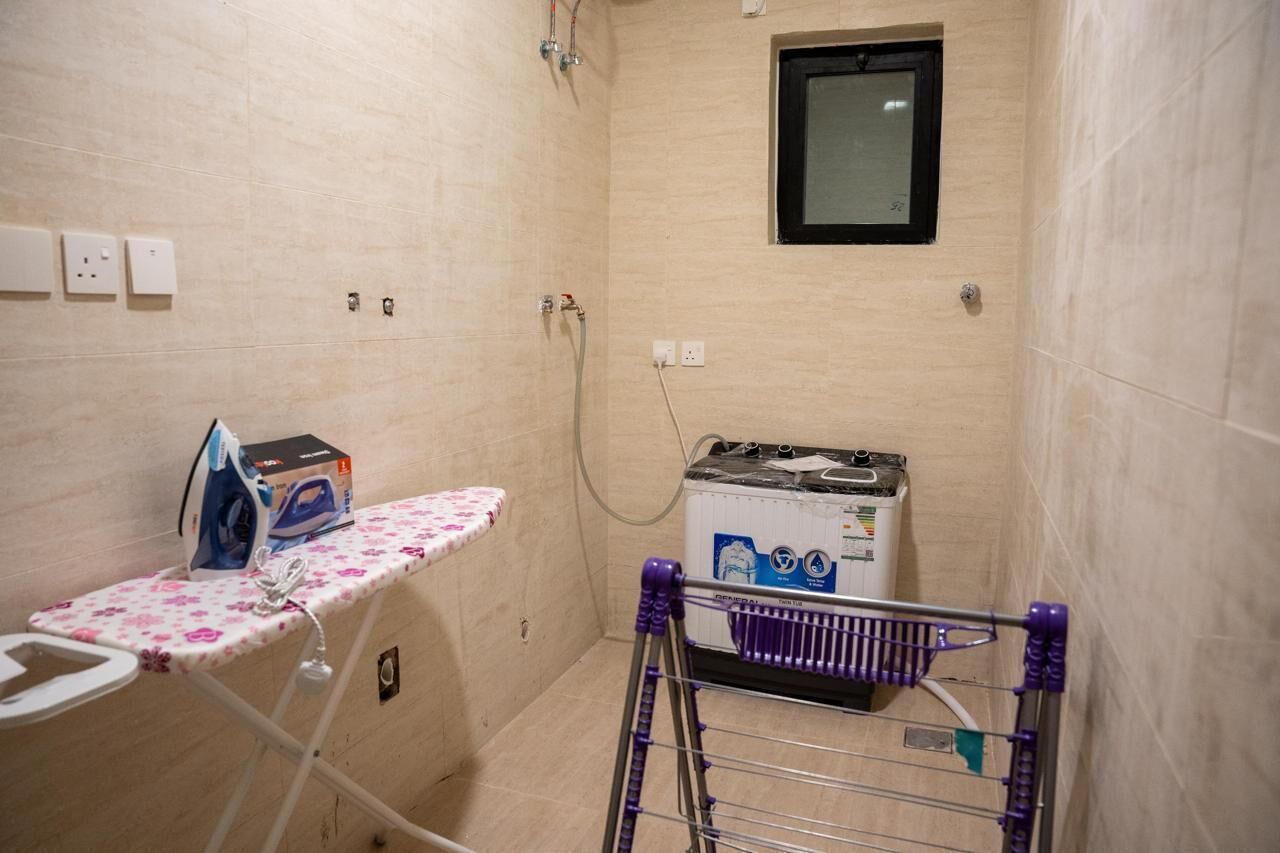 A small laundry room with a washing machine, an ironing board, and a drying rack.