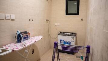 A small laundry room with a washing machine, an ironing board, and a drying rack.