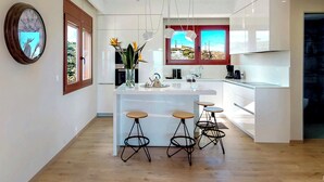 Una cocina moderna con una isla central, taburetes de bar y vistas al exterior a través de un ventanal.