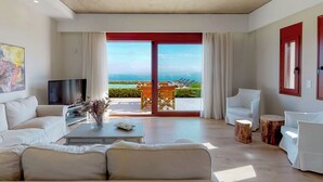 Amplia sala de estar con televisor grande, un sofá y una mesa de centro. Se ve el océano a través de puertas correderas grandes.