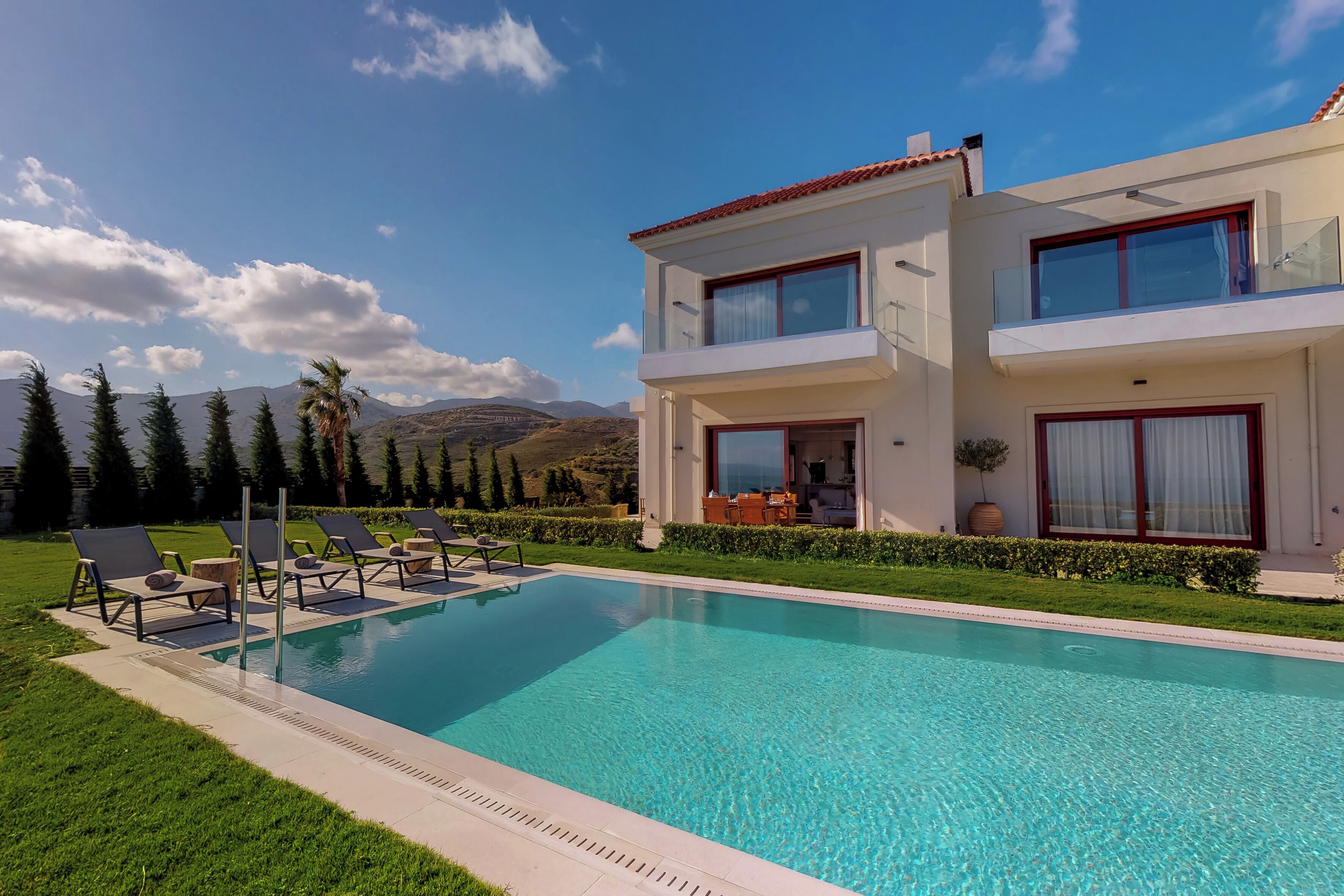 A two-story house with a swimming pool, outdoor seating, and a view of mountains.