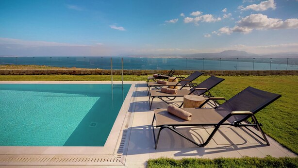 Piscina con sillas de descanso y vista al océano y a las montañas.