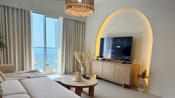 A modern living room with a large TV, comfortable seating, and a view of the city. - Top floor Grande 2BR Luxe Panoramic Sea View Bohemian Style (Dubai)