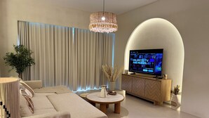 A modern living room with a large flat-screen TV, a sofa, a coffee table, and a decorative plant. - Top floor Grande 2BR Luxe Panoramic Sea View Bohemian Style (Dubai)
