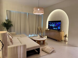 A modern living room with a large flat-screen TV, a sofa, a coffee table, and a decorative plant. - Top floor Grande 2BR Luxe Panoramic Sea View Bohemian Style (Dubai)
