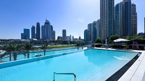 A swimming pool with a city skyline in the background, surrounded by palm trees and modern buildings. - Top floor Grande 2BR Luxe Panoramic Sea View Bohemian Style (Dubai)