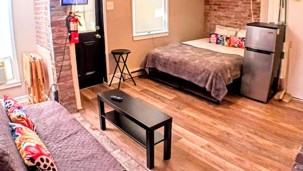 Un espacio habitable compacto con cama, una mesita, un sofá, un televisor y un refrigerador.