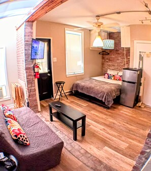 A compact living space with a bed, a small table, a sofa, a TV, and a refrigerator. - Peaceful apartment in Philadelphia perfect for your city getaway (Philadelphia)