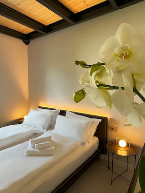 Ein Hotelzimmer mit einem Bett, weißen Kissen, einem Nachttisch mit Lampe und einer großen, weißen Orchidee an der Wand.