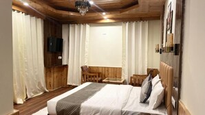 Een slaapkamer met een houten plafond, een bed met witte beddengoed, een houten nachtkastje, een stoel, een klein tafeltje en een aan de muur bevestigde televisie.