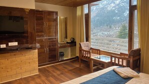 Een kamer met een bed, houten meubels, een televisie en een groot raam met uitzicht op de bergen.