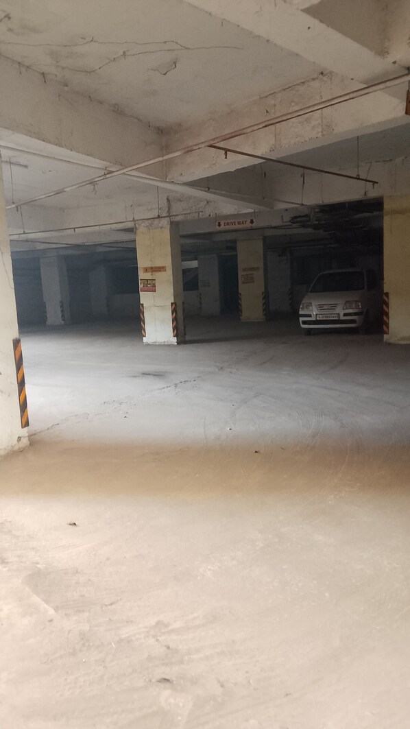 An underground parking garage with concrete pillars, a white car parked in one of the bays, and a 'Drive Way' sign above the entrance. - Hotel Dream (Ahmedabad)