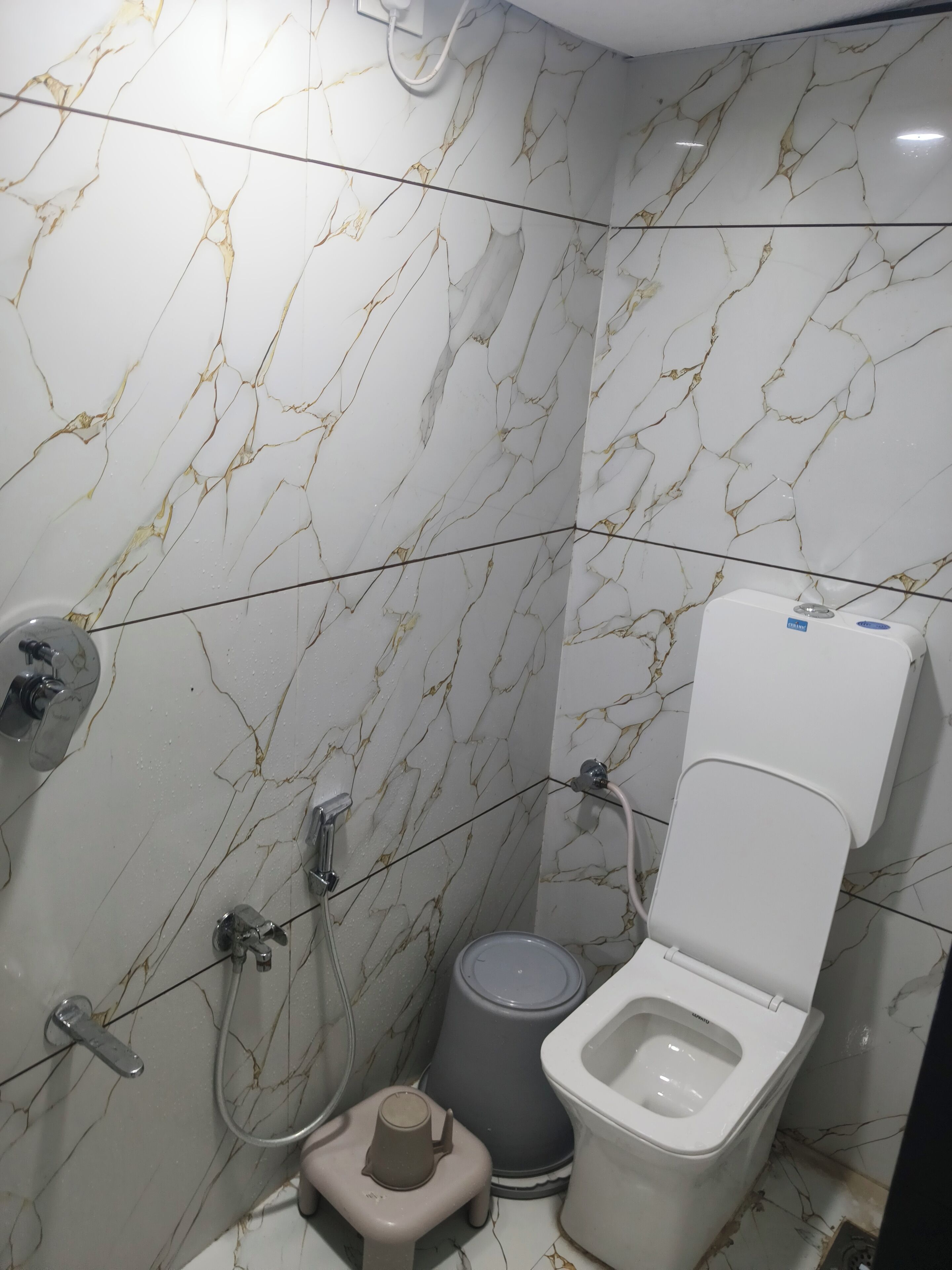 Un baño pequeño con inodoro, bidé, un cubo de basura y cabezal de ducha.