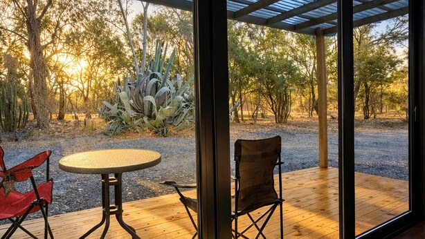 A room with a large glass door leading to an outdoor patio with a wooden table and two chairs.