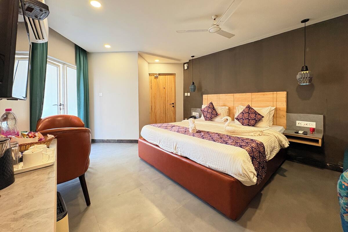 A modern hotel room with a large bed, a desk with a chair, a ceiling fan, and a bedside table with a lamp.