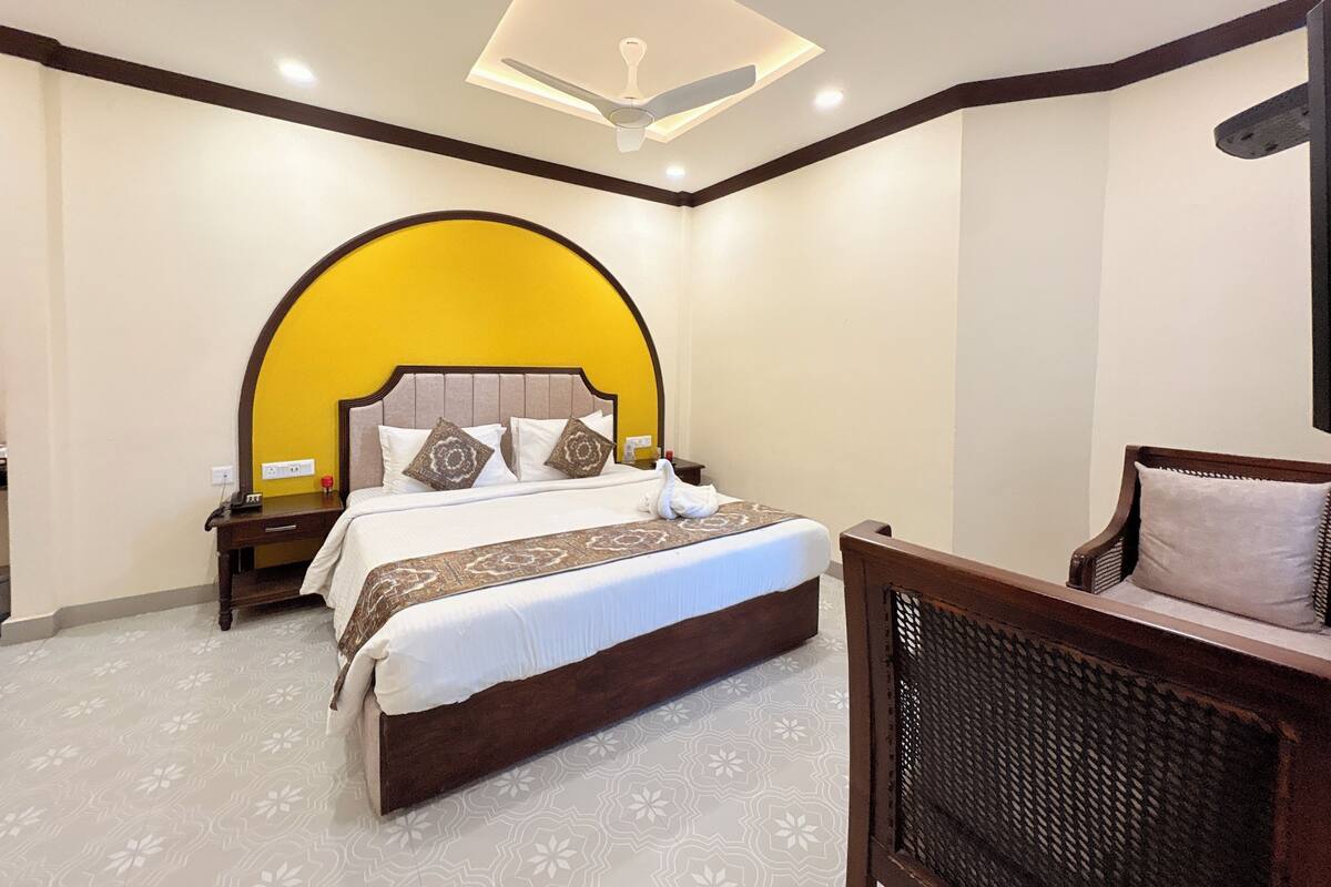 A hotel room with a large bed, a curved yellow wall, a ceiling fan, and a small seating area with a chair and a table.
