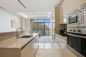 A modern kitchen with a large island, built-in oven, and a view of a cityscape through large windows. - Stunning 2 Bedroom in Palm with private beach (Dubai)