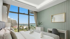 Ein Hotelzimmer mit einem großen Bett, einem Schreibtisch, einem Stuhl und Blick auf Stadt und Meer.