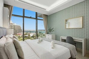 A hotel room with a large bed, a desk, a chair, and a view of the city and sea. - Stunning 2 Bedroom in Palm with private beach (Dubai)