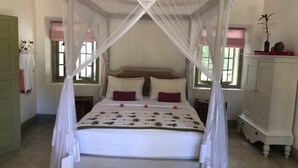Un letto a baldacchino con tende floreali, due cuscini e un comodino con una lampada.