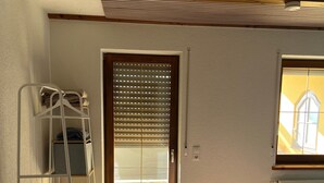 Ein Schlafzimmer mit einem Bett, einer Holzleiter, einer Tür mit Jalousien und einem Fenster mit Blick.