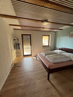 Ein Schlafzimmer mit Holzboden, einem Bett mit Kopfteil, einem Fenster und einer Tür.