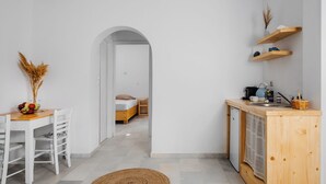A modern, minimalistic room with a wooden dining table, a bed with a white mattress, and a kitchenette with wooden shelves. - Naxos Aethereal view (Naxos)