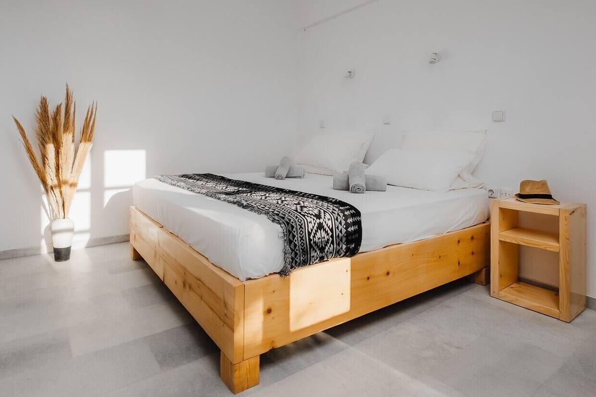 A minimalist bedroom with a wooden bed, white bedding, and a bedside table with a hat.
