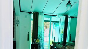 Ein Zimmer mit Fliesenboden, einer Couch, einem Tisch, einem Heizkörper und einem Fenster mit Vorhängen.