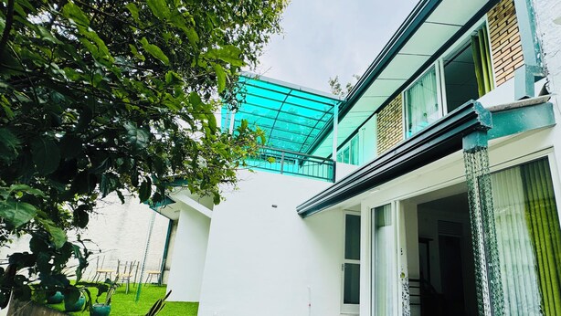 Ein modernes Haus mit weißer Fassade, einem grünen Rasen und einer Glastür, die auf einen Balkon führt.