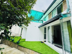 A modern house with a white exterior, a green lawn, and a glass door leading to a balcony. - Charming 3-Bedroom Apartment with Garden in Kandy (Central Province)