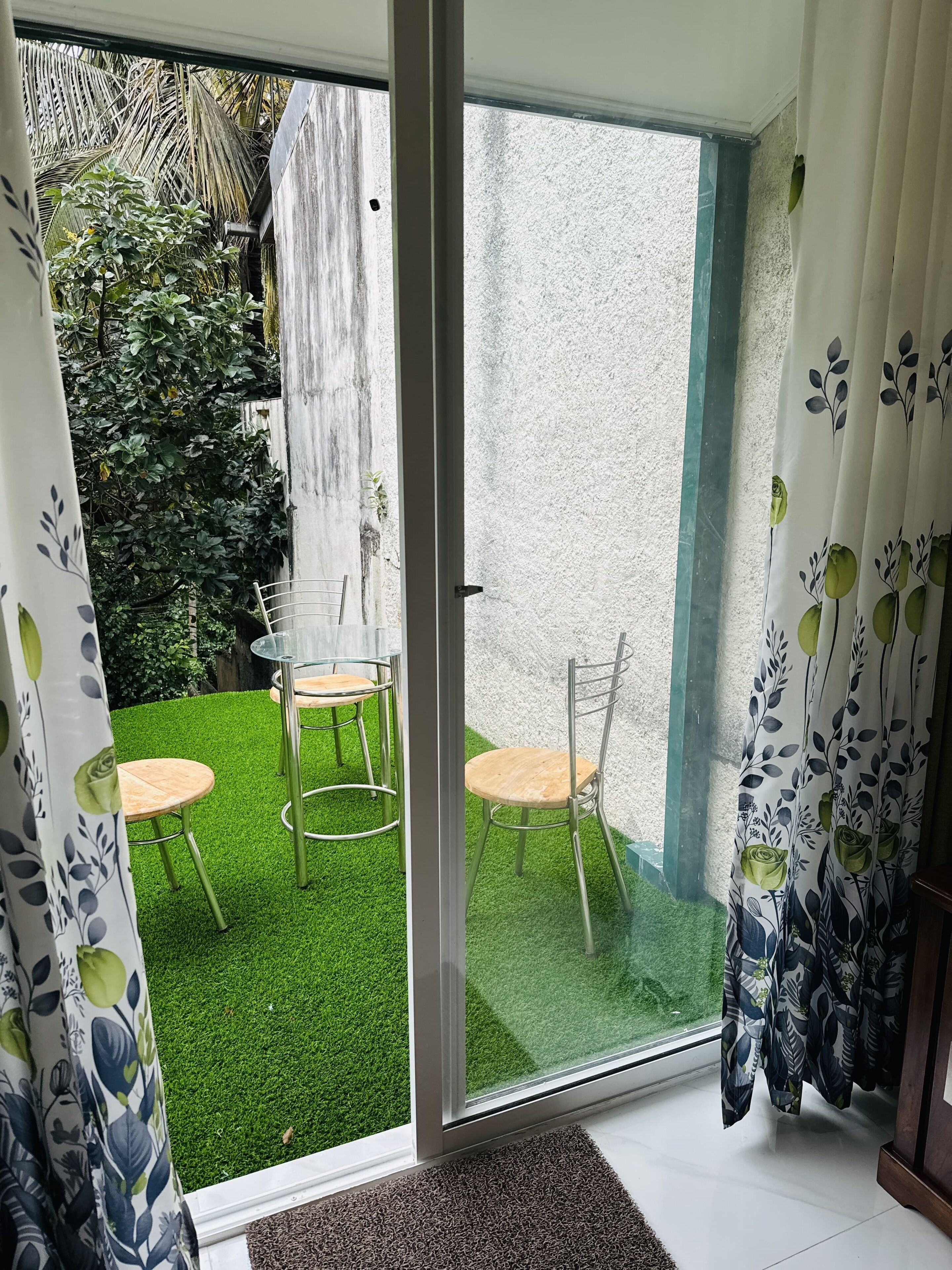 Een kamer met een schuifdeur die uitkomt op een klein buitenruimte met kunstgras en twee stoelen.