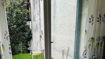 Een kamer met een schuifdeur die uitkomt op een klein buitenruimte met kunstgras en twee stoelen.