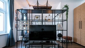 Een moderne woonkamer met een televisie op een zwarte tv-meubel, een glazen salontafel en een prikbordwand met diverse items en foto’s.