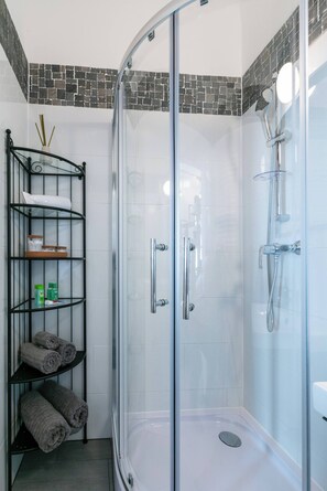 A glass-enclosed shower with a handheld showerhead, a glass door, and a metal shelf unit with towels. - 6 min walk to metro - 3 stops to city center (Wien)