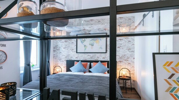 Een moderne slaapkamer met een bed, een wereldkaart aan de muur en een glazen scheiding waarop het woord 'NEW' staat.