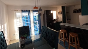 A modern kitchen with dark cabinets, a marble countertop, and a built-in oven. There is a dining area with a blue sofa and two wooden stools. - Charming 2-Bedroom Apartment with Stunning Views in Santiago (Santiago de los Caballeros)