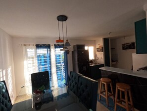 Moderni keittiö, jossa on tummat kaapit, marmoritaso ja sisäänrakennettu uuni. Keittiössä on myös ruokailutila, jossa on sininen sohva ja kaksi puista jakkaraa.