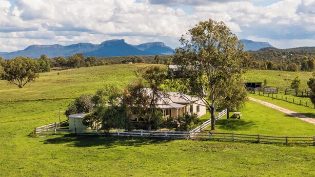 A rural house with a large tree in front, surrounded by a fenced pasture and a mountain in the background. - Mountain-view farmhouse farmstay on the Capertee Valley Bird Trail (Bogee)