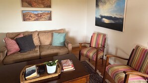 A living room with a brown leather sofa, a striped armchair, and a coffee table with a plant and books. - Mountain-view farmhouse farmstay on the Capertee Valley Bird Trail (Bogee)