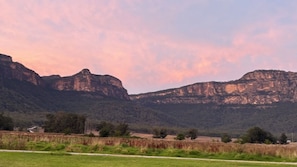 Un paysage comprenant une route, des champs couverts d’herbe et des montagnes.