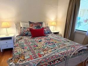 Ein Bett mit farbig gemustertem Überwurf, zwei Nachttischlampen und ein Fenster mit Vorhängen.