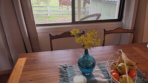 A wooden dining table with a vase of yellow flowers, a candle, and a fruit basket. - Mountain-view farmhouse farmstay on the Capertee Valley Bird Trail (Bogee)