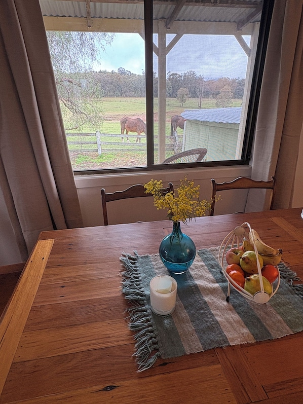 Un tavolo da pranzo in legno con un vaso di fiori gialli, una candela e un cesto di frutta.