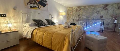 A modern bedroom with a large bed, a nightstand, a lamp, and a stone wall.